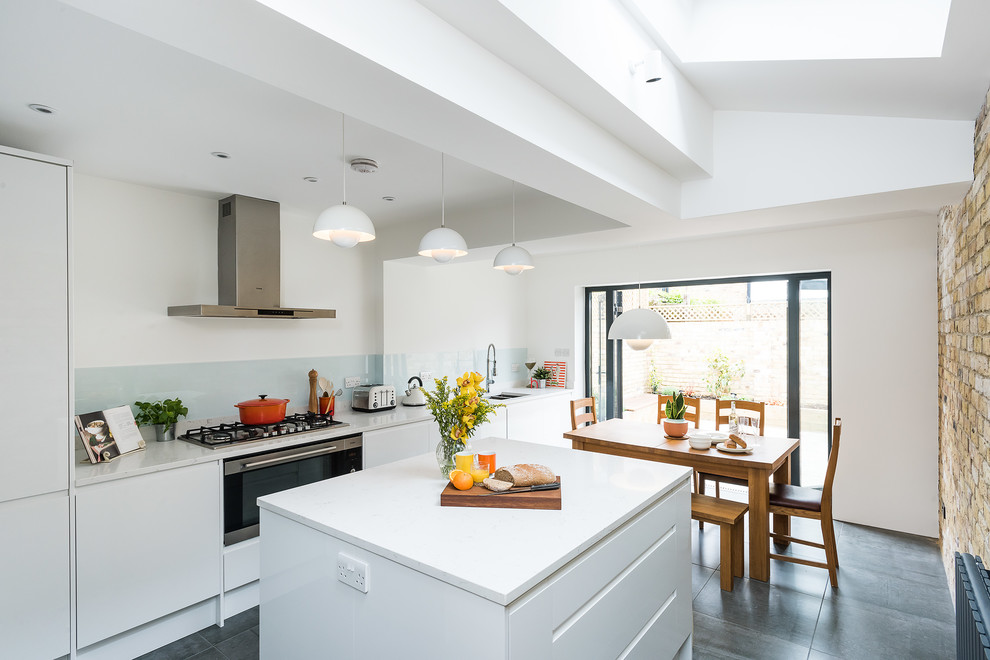 Medium sized contemporary l-shaped open plan kitchen in London with a double-bowl sink, flat-panel cabinets, white cabinets, marble worktops, green splashback, glass sheet splashback, stainless steel appliances, porcelain flooring, an island and grey floors.
