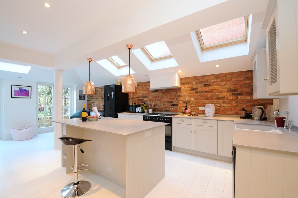 Example of a danish l-shaped light wood floor kitchen design in London with a farmhouse sink, shaker cabinets, white cabinets, black appliances and an island