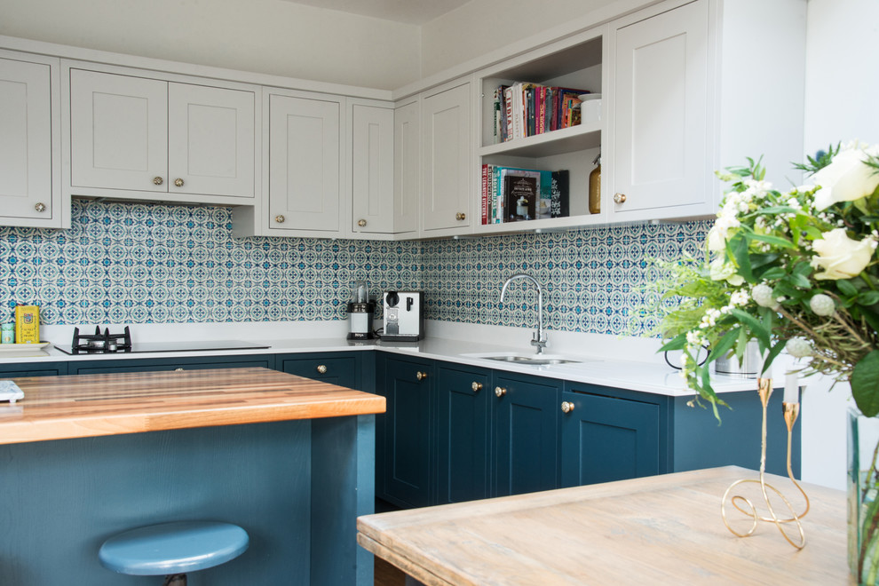 Photo of a medium sized traditional l-shaped kitchen/diner in Edinburgh with shaker cabinets, blue cabinets, ceramic splashback, an island, a submerged sink, composite countertops, white splashback and dark hardwood flooring.