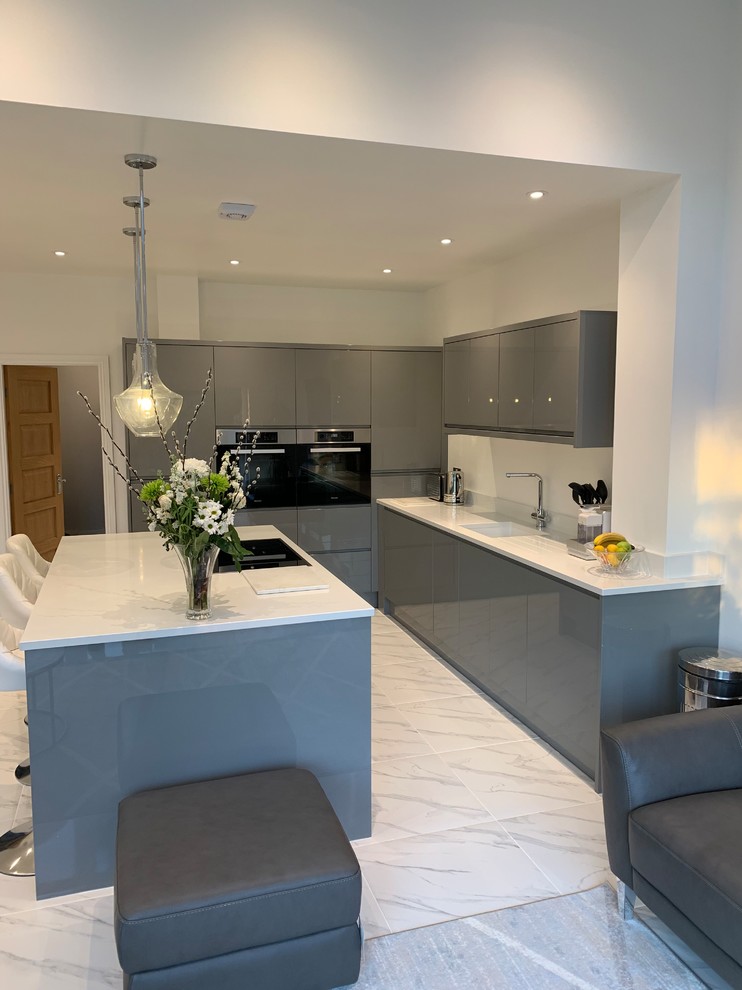 Photo of a medium sized contemporary l-shaped open plan kitchen in West Midlands with a submerged sink, flat-panel cabinets, grey cabinets, granite worktops, white splashback, integrated appliances, porcelain flooring, an island, white floors and white worktops.