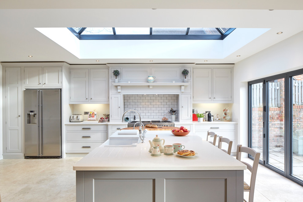 This is an example of a large traditional single-wall kitchen/diner in Wiltshire with a belfast sink, recessed-panel cabinets, grey cabinets, engineered stone countertops, beige splashback, stone slab splashback, stainless steel appliances, limestone flooring and a breakfast bar.