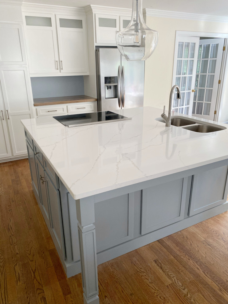 This is an example of a contemporary l-shaped kitchen in Atlanta with a double-bowl sink, shaker cabinets, white cabinets, engineered stone countertops, grey splashback, cement tile splashback, stainless steel appliances, dark hardwood flooring, an island, brown floors and white worktops.