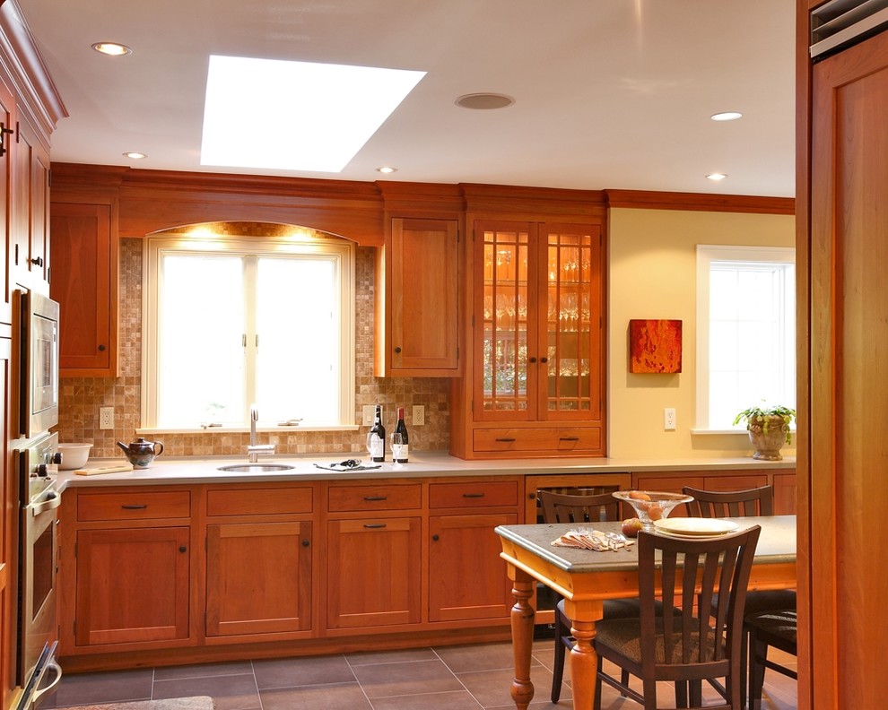 Inredning av ett klassiskt kök och matrum, med en undermonterad diskho, luckor med infälld panel, skåp i mellenmörkt trä, bänkskiva i koppar, beige stänkskydd, stänkskydd i stenkakel och rostfria vitvaror