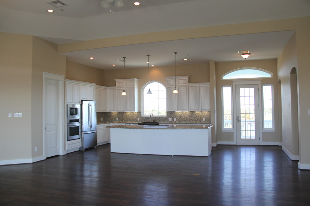 Foto på ett mellanstort maritimt kök, med en undermonterad diskho, luckor med profilerade fronter, vita skåp, granitbänkskiva, flerfärgad stänkskydd, mörkt trägolv, en köksö, rostfria vitvaror och stänkskydd i mosaik