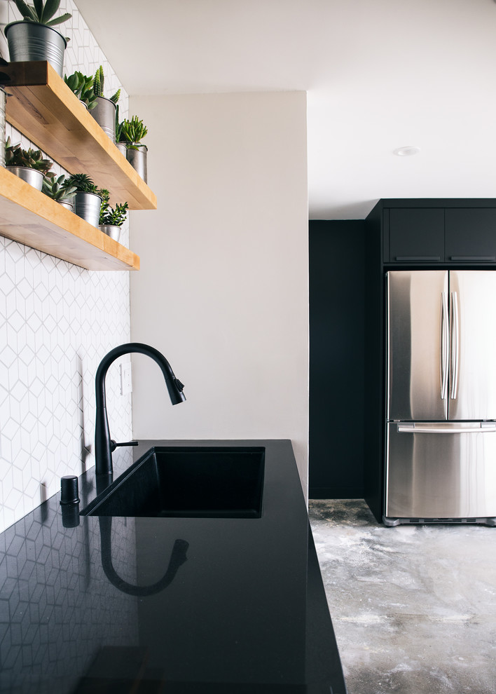 Small contemporary galley kitchen/diner in San Francisco with a submerged sink, flat-panel cabinets, black cabinets, quartz worktops, white splashback, ceramic splashback, stainless steel appliances, concrete flooring, an island, grey floors and black worktops.