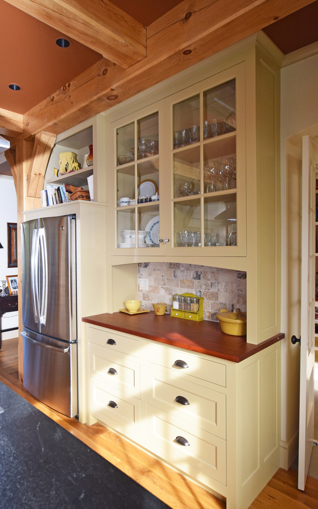 Foto på ett stort lantligt kök, med en enkel diskho, luckor med profilerade fronter, gula skåp, träbänkskiva, beige stänkskydd, stänkskydd i stenkakel, rostfria vitvaror, ljust trägolv och flera köksöar