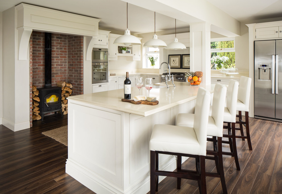 Foto de cocina comedor clásica con armarios estilo shaker, puertas de armario blancas, electrodomésticos de acero inoxidable y suelo de madera oscura