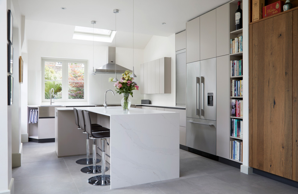 Trendy l-shaped gray floor kitchen photo in London with flat-panel cabinets, gray cabinets, stainless steel appliances, an island and white countertops