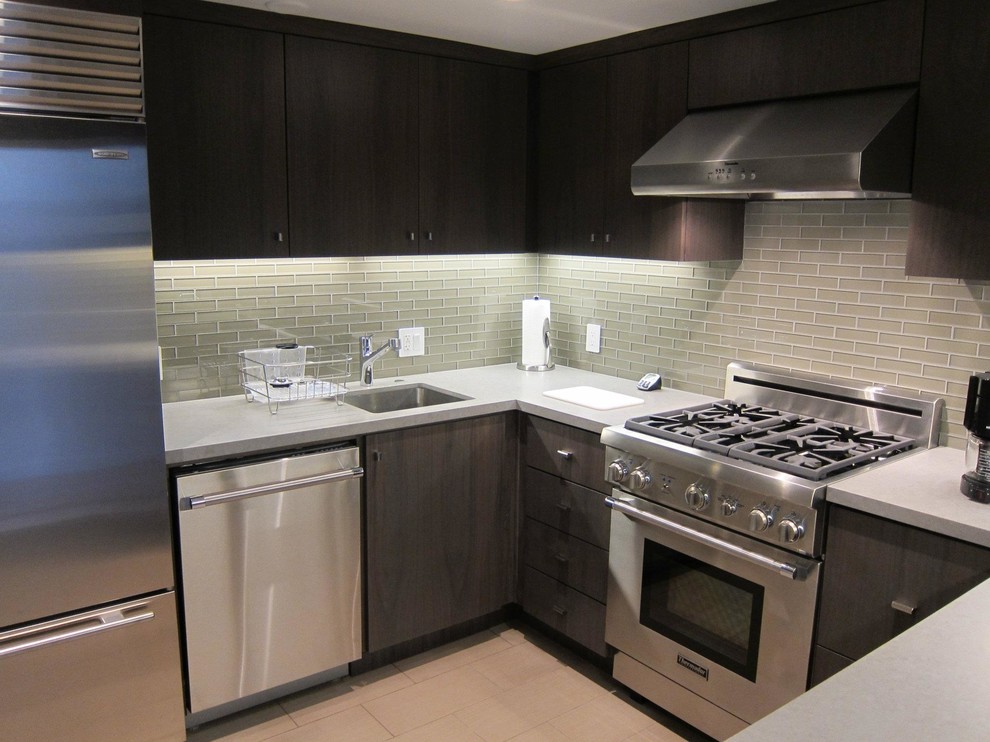 This is an example of a large modern u-shaped enclosed kitchen in San Francisco with flat-panel cabinets, dark wood cabinets, a breakfast bar, a submerged sink, green splashback, glass tiled splashback and stainless steel appliances.