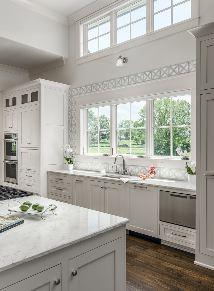 Classic l-shaped open plan kitchen in Nashville with a submerged sink, beaded cabinets, white cabinets, engineered stone countertops, white splashback, stone tiled splashback, stainless steel appliances, dark hardwood flooring, an island, brown floors and white worktops.