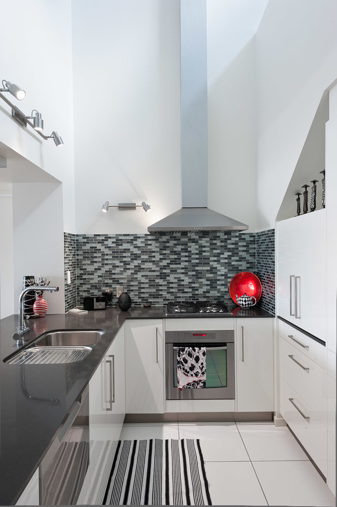 Photo of a medium sized contemporary l-shaped kitchen/diner in Brisbane with a submerged sink, flat-panel cabinets, white cabinets, quartz worktops, grey splashback, matchstick tiled splashback, a breakfast bar and white floors.