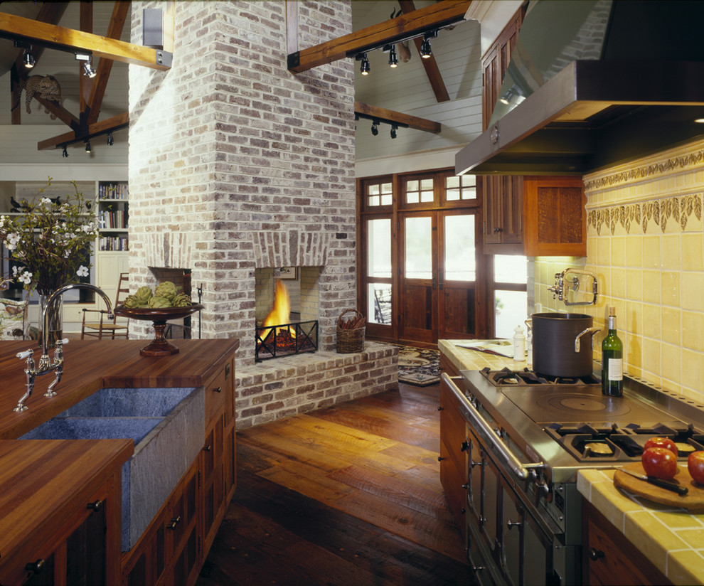 Bild på ett mellanstort lantligt kök, med skåp i mellenmörkt trä, kaklad bänkskiva, gult stänkskydd, rostfria vitvaror, en rustik diskho, luckor med infälld panel, stänkskydd i keramik, mörkt trägolv och en köksö