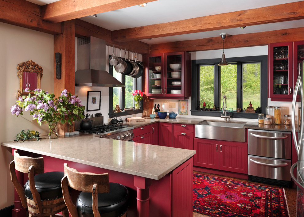 Rustik inredning av ett mellanstort u-kök, med rostfria vitvaror, en rustik diskho, röda skåp, brunt golv, granitbänkskiva, mörkt trägolv och luckor med infälld panel