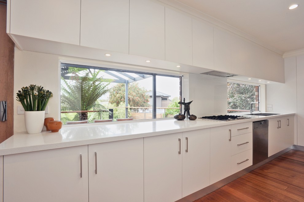 Design ideas for a large contemporary galley enclosed kitchen in Melbourne with a double-bowl sink, white cabinets, engineered stone countertops, stainless steel appliances, light hardwood flooring and an island.