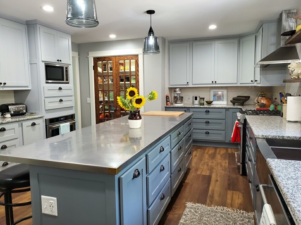 Example of a mid-sized farmhouse u-shaped dark wood floor and brown floor enclosed kitchen design in Omaha with a farmhouse sink, shaker cabinets, blue cabinets, quartz countertops, subway tile backsplash, stainless steel appliances, an island and gray countertops