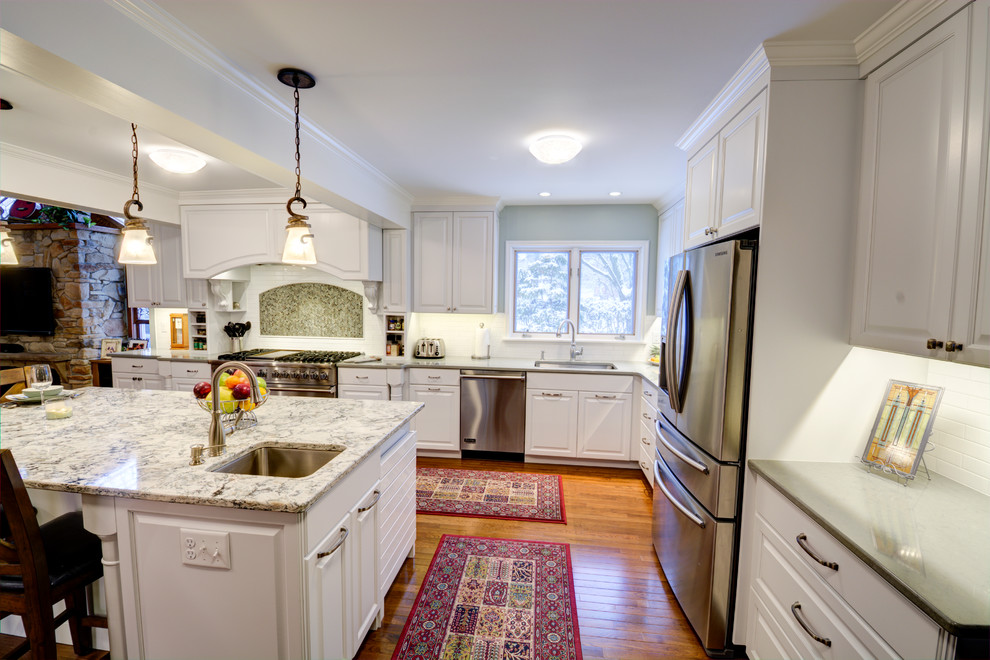 Example of a mid-sized classic u-shaped medium tone wood floor enclosed kitchen design in Detroit with an undermount sink, white backsplash, subway tile backsplash, stainless steel appliances, raised-panel cabinets, white cabinets, granite countertops and an island