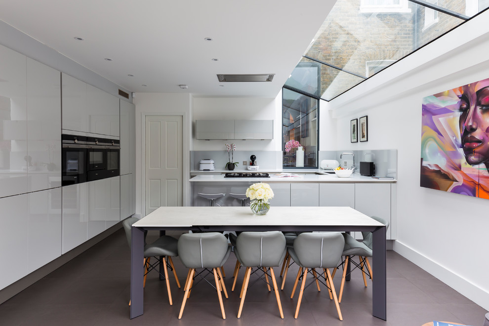 Mittelgroße Moderne Wohnküche mit flächenbündigen Schrankfronten, grauen Schränken, Halbinsel, Glasrückwand und schwarzen Elektrogeräten in London