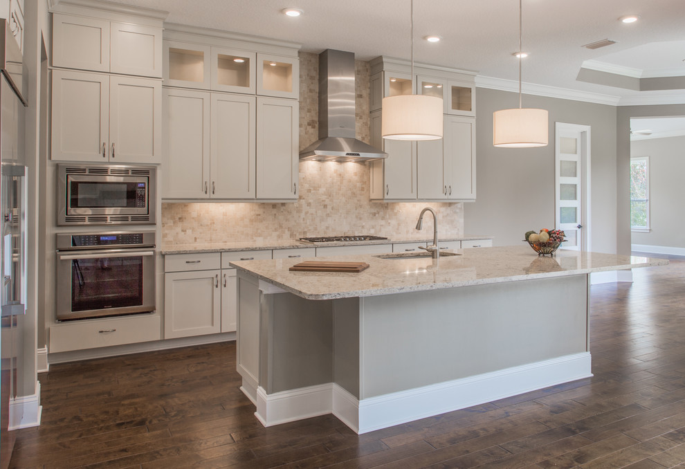 Photo of a classic kitchen/diner in Jacksonville with a submerged sink, shaker cabinets, beige cabinets, beige splashback, stainless steel appliances, dark hardwood flooring and an island.