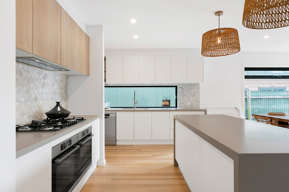 This is an example of a contemporary u-shaped open plan kitchen in Melbourne with a submerged sink, flat-panel cabinets, white cabinets, engineered stone countertops, grey splashback, stone tiled splashback, stainless steel appliances, medium hardwood flooring, an island and grey worktops.