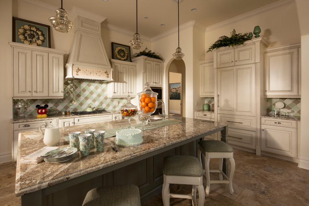 Example of a large tuscan l-shaped brown floor and travertine floor enclosed kitchen design in Orlando with raised-panel cabinets, white cabinets, multicolored backsplash, stainless steel appliances, an island, granite countertops and ceramic backsplash