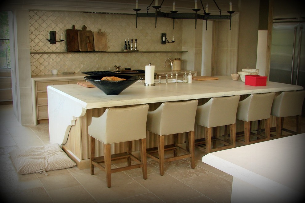 На фото: большая прямая кухня-гостиная в средиземноморском стиле с врезной мойкой, светлыми деревянными фасадами, столешницей из известняка, техникой из нержавеющей стали, полом из травертина и двумя и более островами с