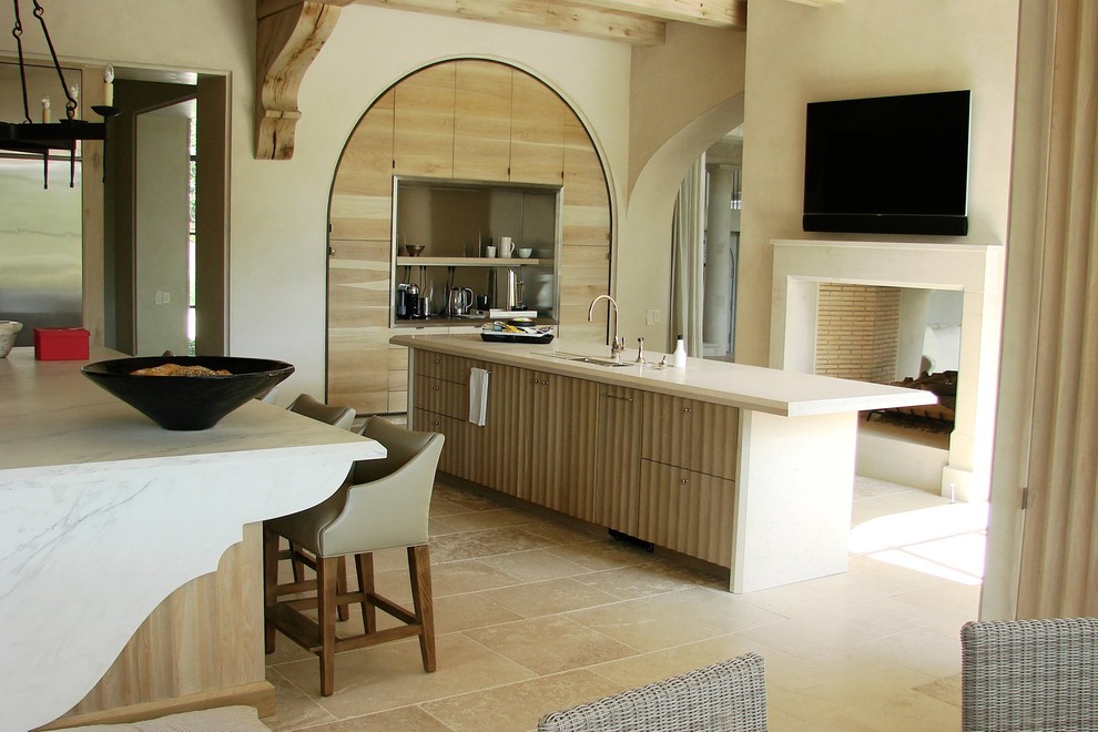 Immagine di una grande cucina mediterranea con lavello sottopiano, ante in legno chiaro, top in pietra calcarea, elettrodomestici in acciaio inossidabile, pavimento in travertino e 2 o più isole