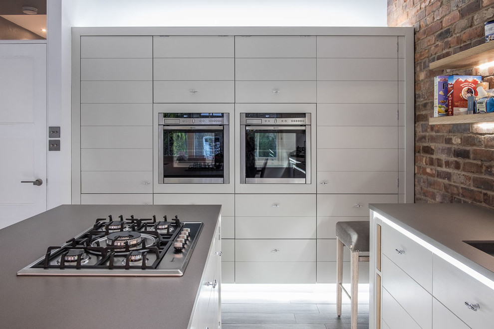 Inspiration for a medium sized modern open plan kitchen in London with a built-in sink, flat-panel cabinets, white cabinets, composite countertops, brick splashback, stainless steel appliances, porcelain flooring, an island, grey floors and grey worktops.