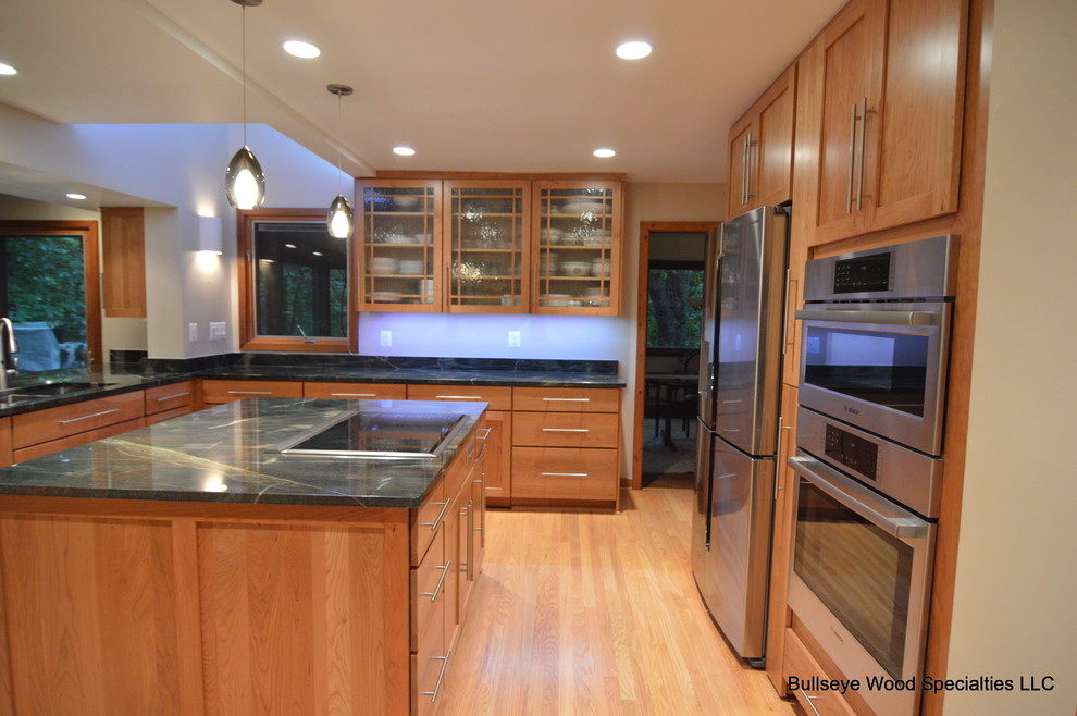 Photo of a large classic u-shaped kitchen/diner in DC Metro with a double-bowl sink, shaker cabinets, medium wood cabinets, granite worktops, green splashback, stainless steel appliances, light hardwood flooring and an island.