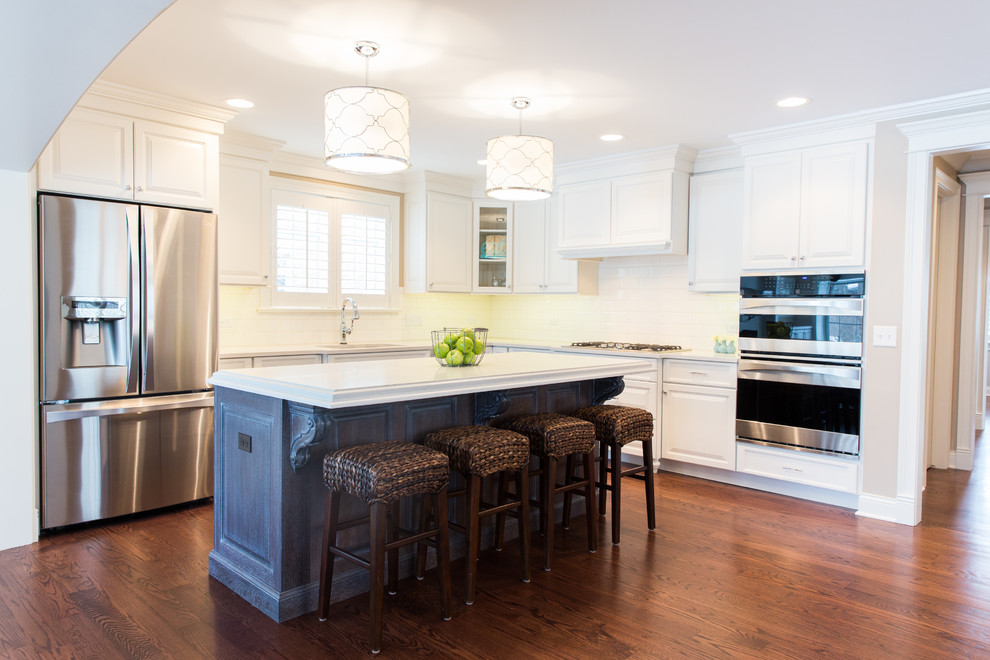 Mid-sized transitional l-shaped medium tone wood floor and brown floor eat-in kitchen photo in Chicago with an undermount sink, raised-panel cabinets, white cabinets, quartz countertops, white backsplash, subway tile backsplash, stainless steel appliances, an island and white countertops