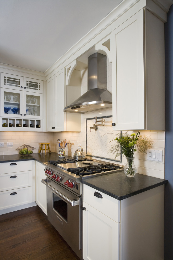 Example of a mid-sized classic u-shaped medium tone wood floor and brown floor eat-in kitchen design in Chicago with stainless steel appliances, subway tile backsplash, soapstone countertops, white cabinets, white backsplash, glass-front cabinets, a farmhouse sink and white countertops