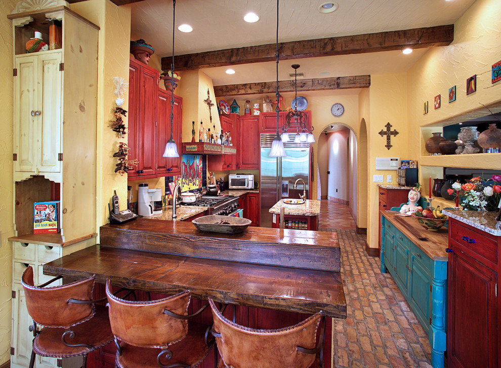 タンパにあるサンタフェスタイルのおしゃれな独立型キッチン (赤いキャビネット、レイズドパネル扉のキャビネット、木材カウンター、シルバーの調理設備、レンガの床) の写真
