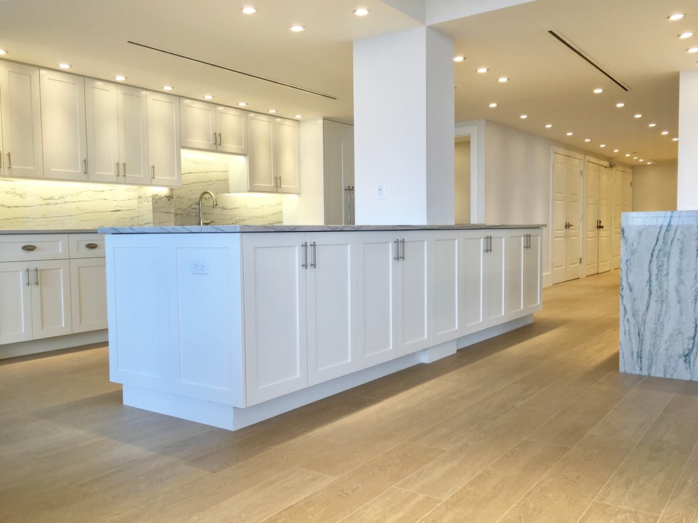 This is an example of a large traditional galley open plan kitchen in Miami with a submerged sink, shaker cabinets, white cabinets, marble worktops, grey splashback, marble splashback, stainless steel appliances, light hardwood flooring, an island and beige floors.
