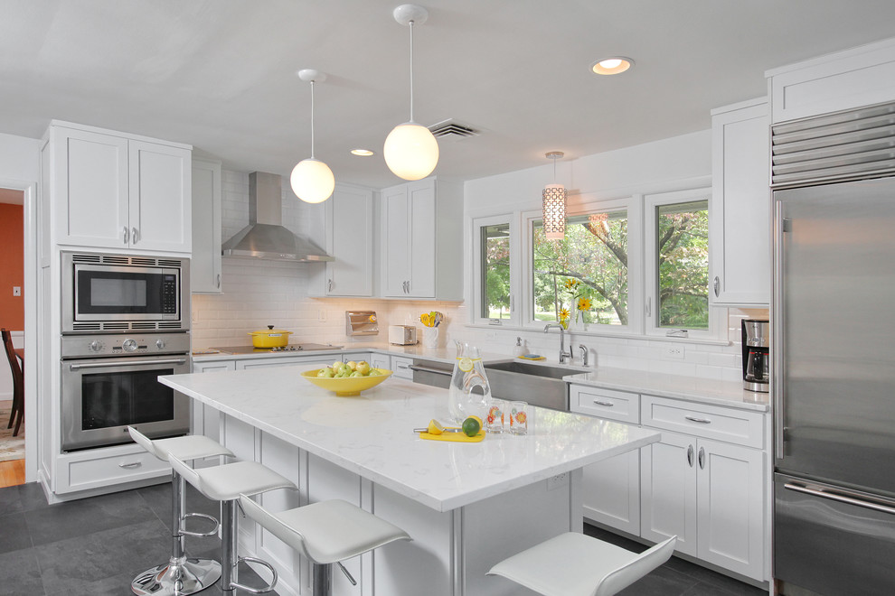 Mid-sized transitional l-shaped slate floor open concept kitchen photo in Philadelphia with a farmhouse sink, shaker cabinets, white cabinets, white backsplash, subway tile backsplash, stainless steel appliances, an island and marble countertops