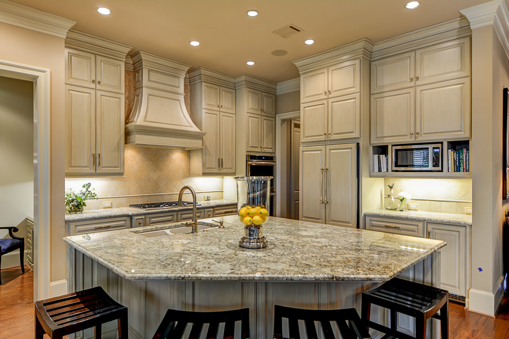 Example of a mid-sized classic l-shaped medium tone wood floor eat-in kitchen design in Austin with an undermount sink, beige cabinets, granite countertops, beige backsplash, stone tile backsplash, paneled appliances and an island