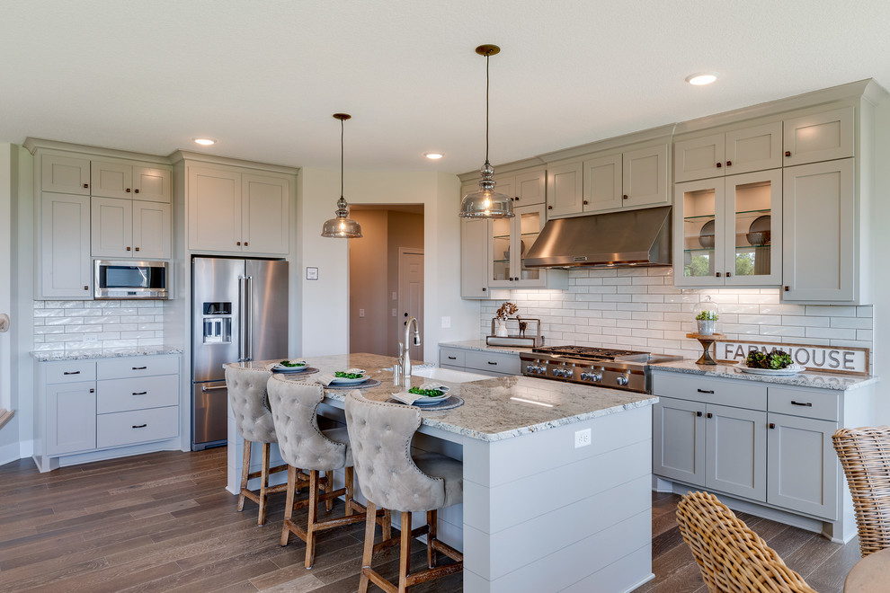 Inspiration for a farmhouse medium tone wood floor and brown floor eat-in kitchen remodel in Minneapolis with a farmhouse sink, glass-front cabinets, gray cabinets, white backsplash, subway tile backsplash, stainless steel appliances, an island and multicolored countertops