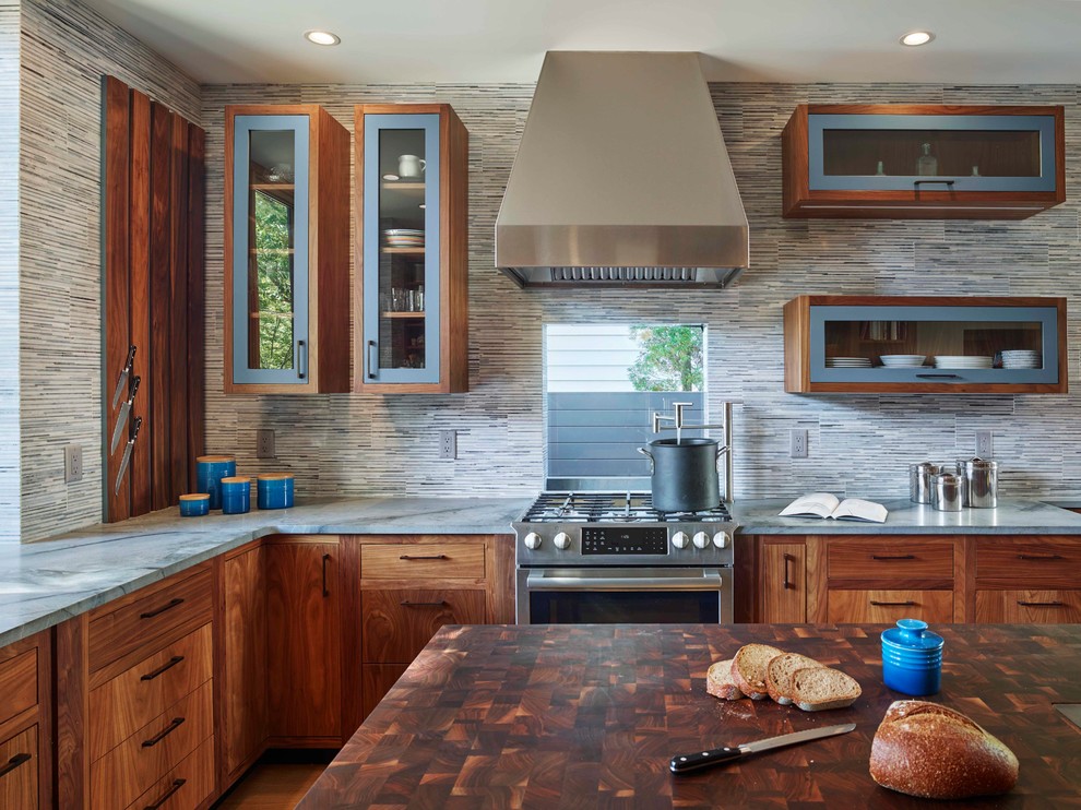Modern inredning av ett mellanstort l-kök, med skåp i mellenmörkt trä, grått stänkskydd, stänkskydd i stenkakel, rostfria vitvaror, ljust trägolv, en köksö, släta luckor och brunt golv
