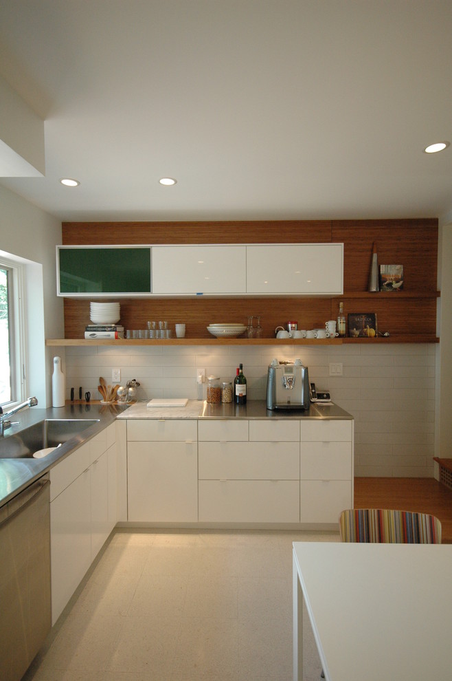 Modern inredning av ett kök, med bänkskiva i rostfritt stål, en integrerad diskho, släta luckor, vita skåp och rostfria vitvaror