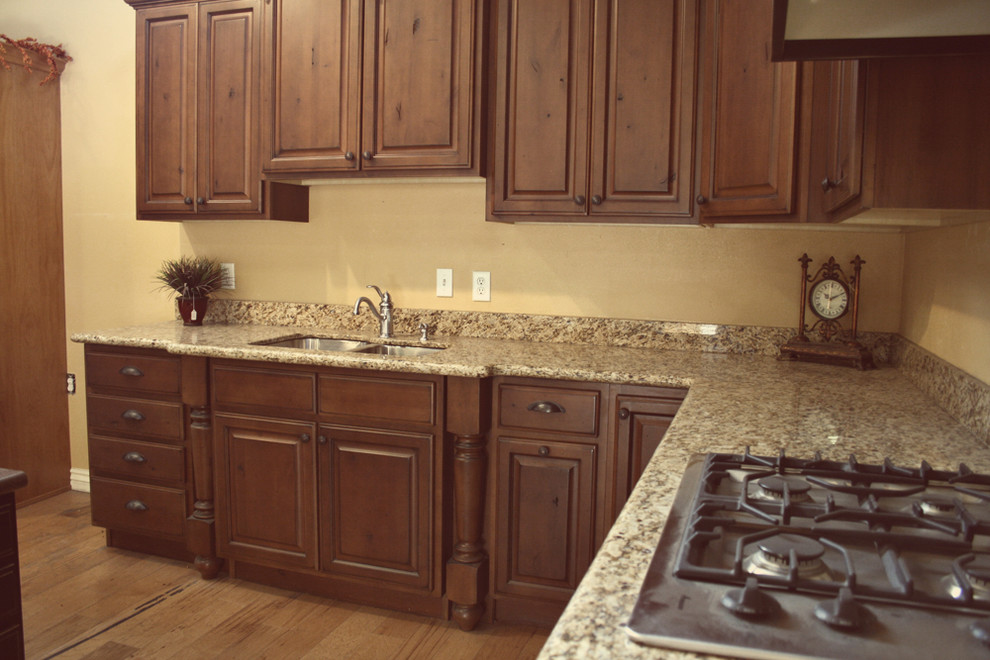 Klassisk inredning av ett kök, med en undermonterad diskho, luckor med upphöjd panel, skåp i mörkt trä, granitbänkskiva och beige stänkskydd
