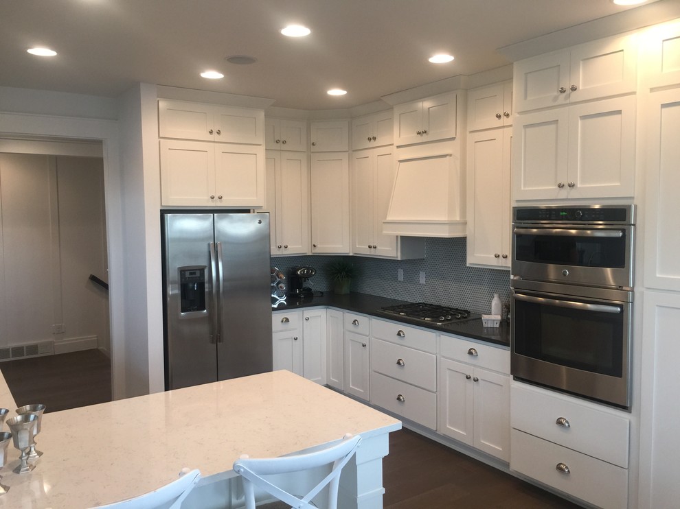 Modern inredning av ett mellanstort kök, med vita skåp, rostfria vitvaror, blått stänkskydd, stänkskydd i mosaik, skåp i shakerstil, bänkskiva i kvartsit, mörkt trägolv, en halv köksö och brunt golv