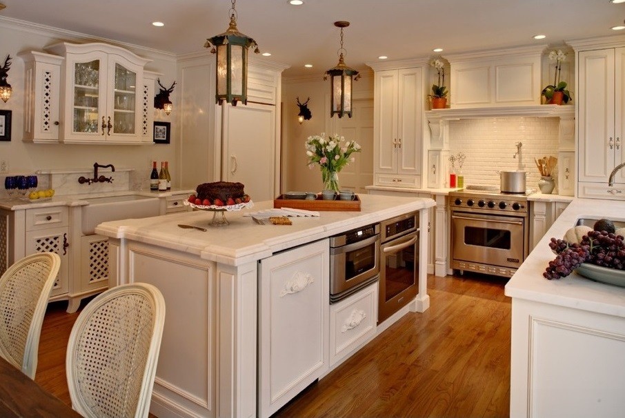 Inredning av ett klassiskt mellanstort kök, med en undermonterad diskho, luckor med infälld panel, vita skåp, marmorbänkskiva, stänkskydd i stenkakel, rostfria vitvaror, ljust trägolv och en köksö