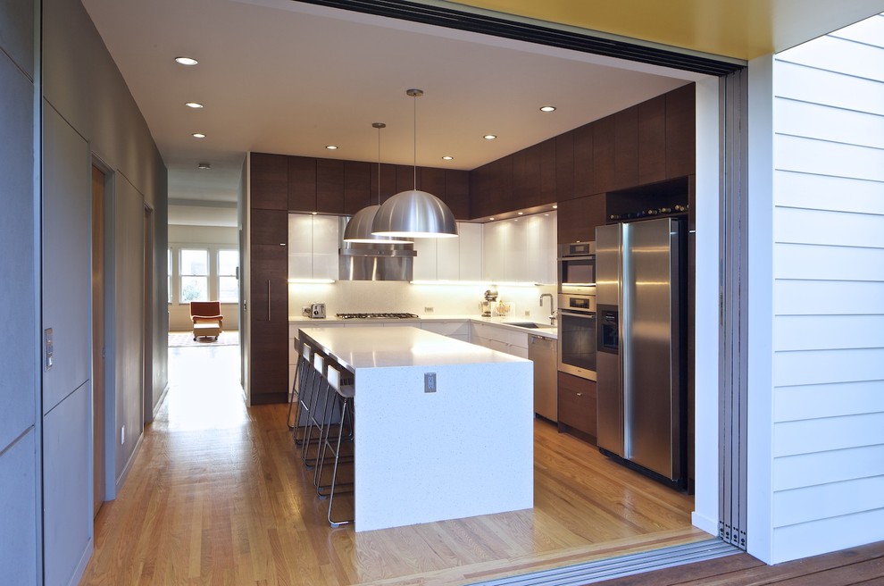 Exemple d'une cuisine moderne en L fermée avec un électroménager en acier inoxydable, un placard à porte plane, des portes de placard blanches, un plan de travail en quartz modifié et une crédence blanche.