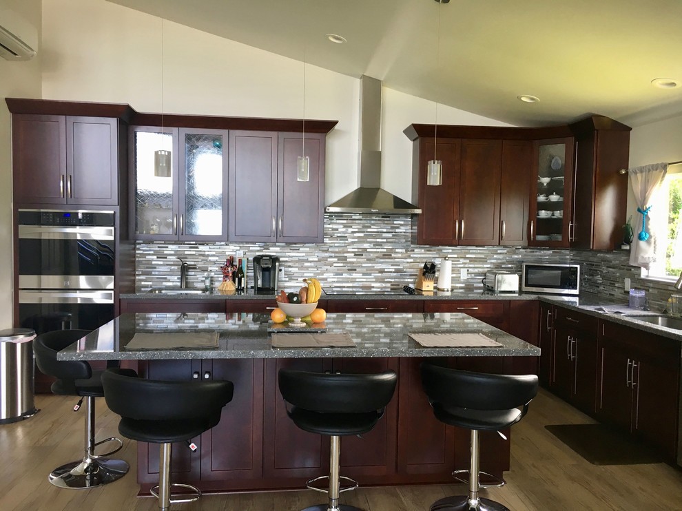 This is an example of a medium sized contemporary l-shaped kitchen/diner in Hawaii with a submerged sink, shaker cabinets, dark wood cabinets, engineered stone countertops, multi-coloured splashback, glass tiled splashback, stainless steel appliances, vinyl flooring, an island and brown floors.