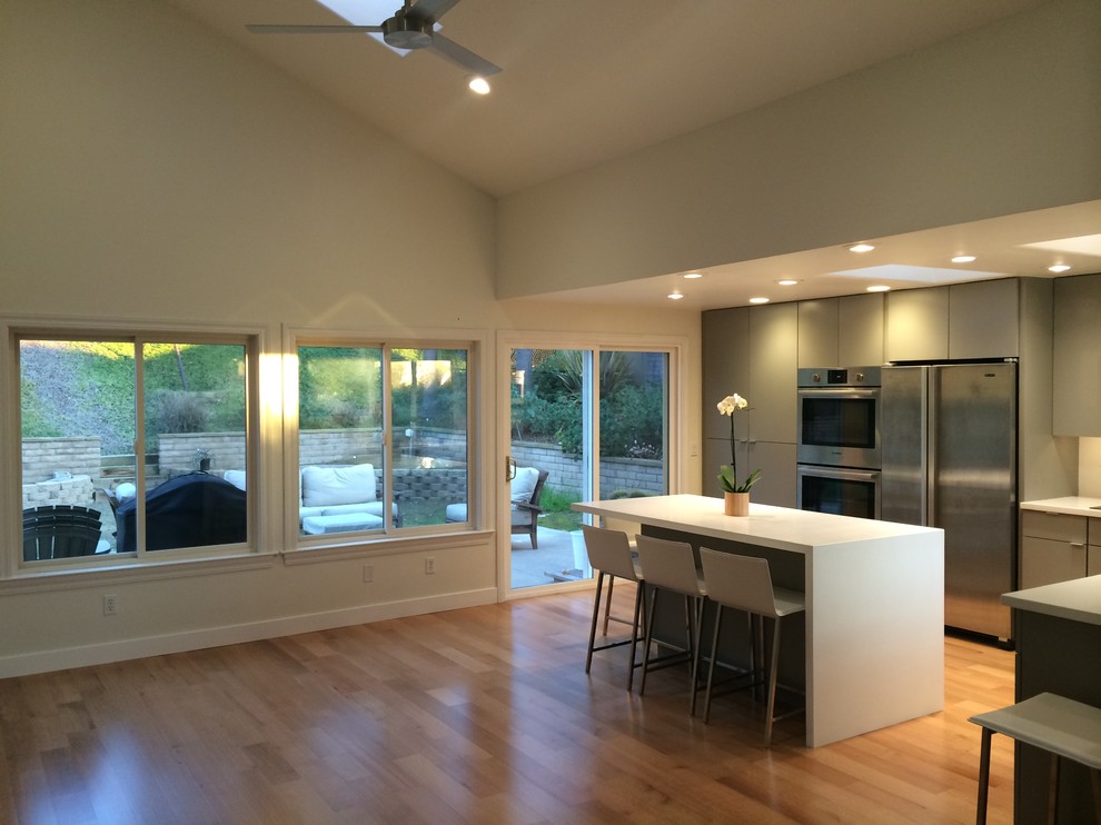 Example of a mid-sized trendy l-shaped light wood floor open concept kitchen design in San Diego with a single-bowl sink, flat-panel cabinets, gray cabinets, quartz countertops, white backsplash, stainless steel appliances and an island