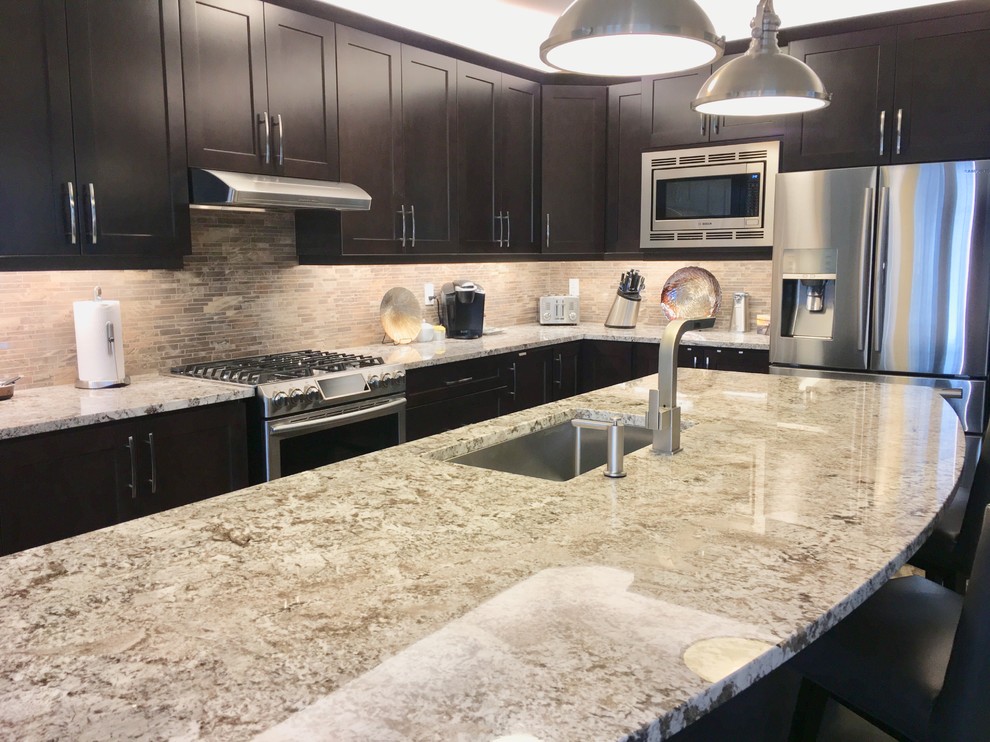 Modern inredning av ett avskilt, stort vit vitt l-kök, med en undermonterad diskho, skåp i shakerstil, skåp i mörkt trä, granitbänkskiva, brunt stänkskydd, stänkskydd i porslinskakel, rostfria vitvaror, klinkergolv i porslin, en köksö och brunt golv