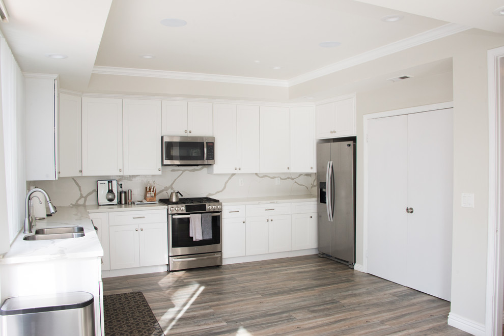 Modern inredning av ett mellanstort vit vitt kök, med en dubbel diskho, släta luckor, vita skåp, marmorbänkskiva, vitt stänkskydd, stänkskydd i stenkakel, rostfria vitvaror, ljust trägolv och grått golv
