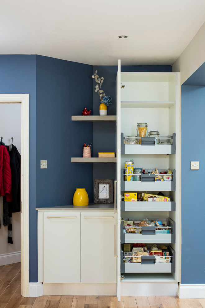 Cette image montre une cuisine américaine minimaliste en L avec un évier 2 bacs, un placard à porte plane, des portes de placard bleues, un plan de travail en surface solide et parquet clair.