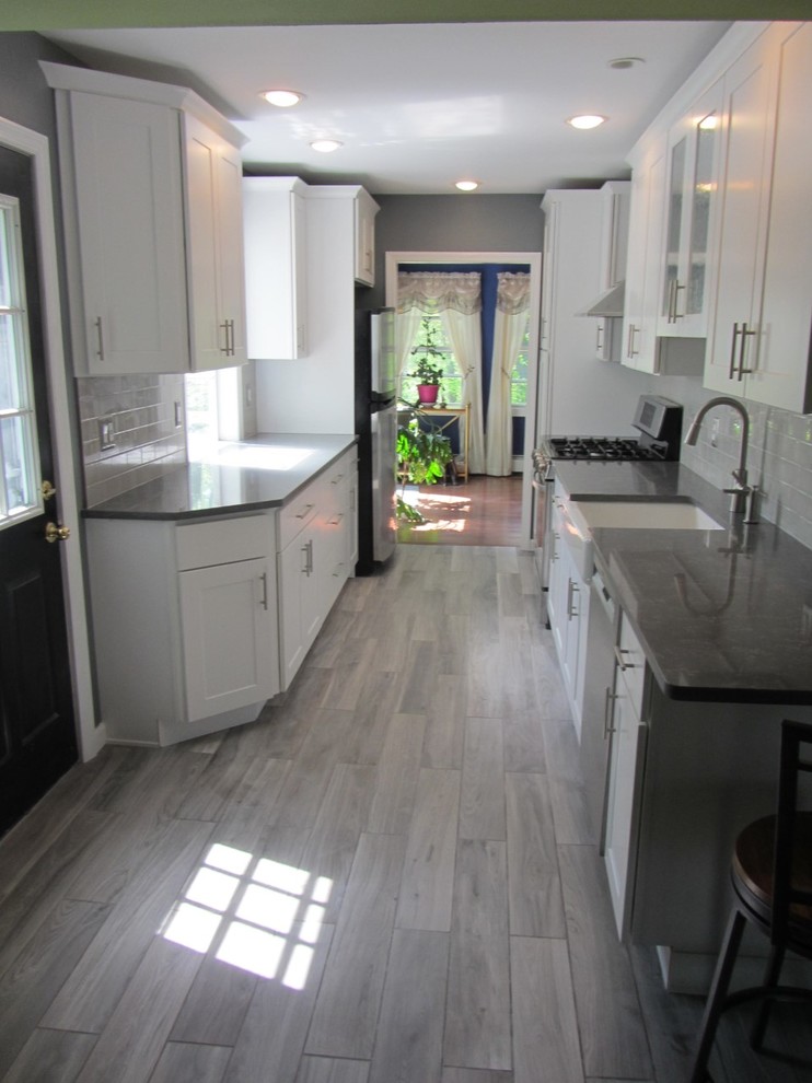 Mid-sized trendy galley porcelain tile and gray floor eat-in kitchen photo in Newark with a farmhouse sink, shaker cabinets, white cabinets, quartzite countertops, gray backsplash, ceramic backsplash and stainless steel appliances