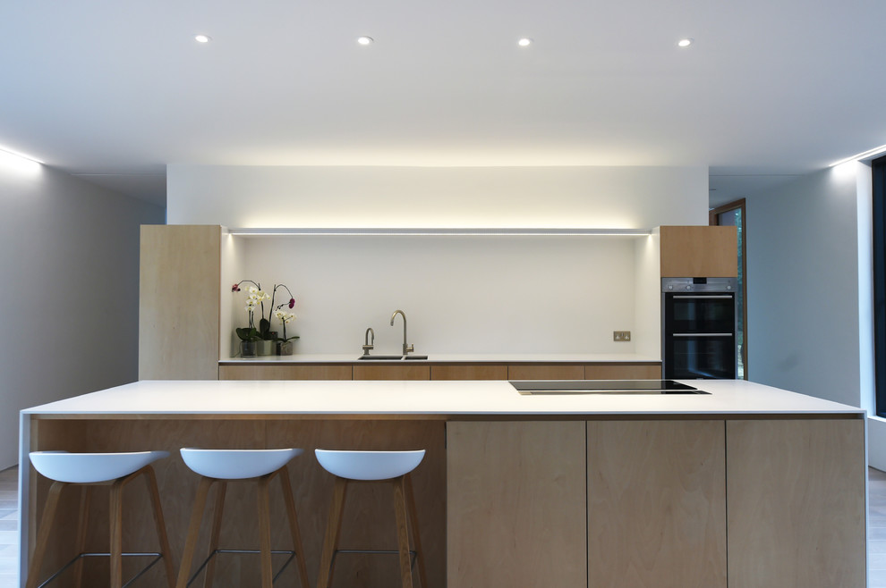 Medium sized modern u-shaped enclosed kitchen in Surrey with a submerged sink, flat-panel cabinets, light wood cabinets, a breakfast bar and white splashback.