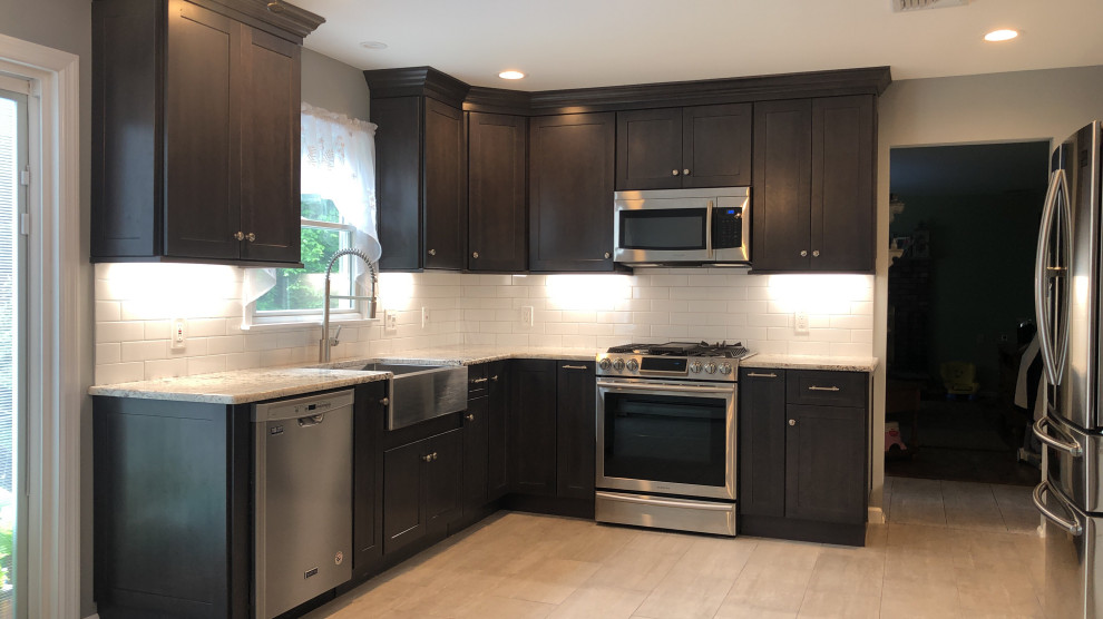 Example of a large minimalist l-shaped porcelain tile kitchen design in Newark with a farmhouse sink, shaker cabinets, dark wood cabinets, quartzite countertops, white backsplash, ceramic backsplash and stainless steel appliances