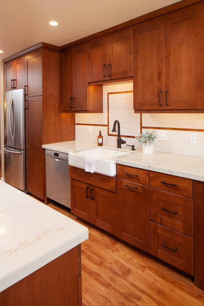 Foto på ett mellanstort 60 tals vit kök, med en rustik diskho, skåp i shakerstil, bruna skåp, bänkskiva i kvarts, vitt stänkskydd, stänkskydd i keramik, rostfria vitvaror, mellanmörkt trägolv, en köksö och brunt golv